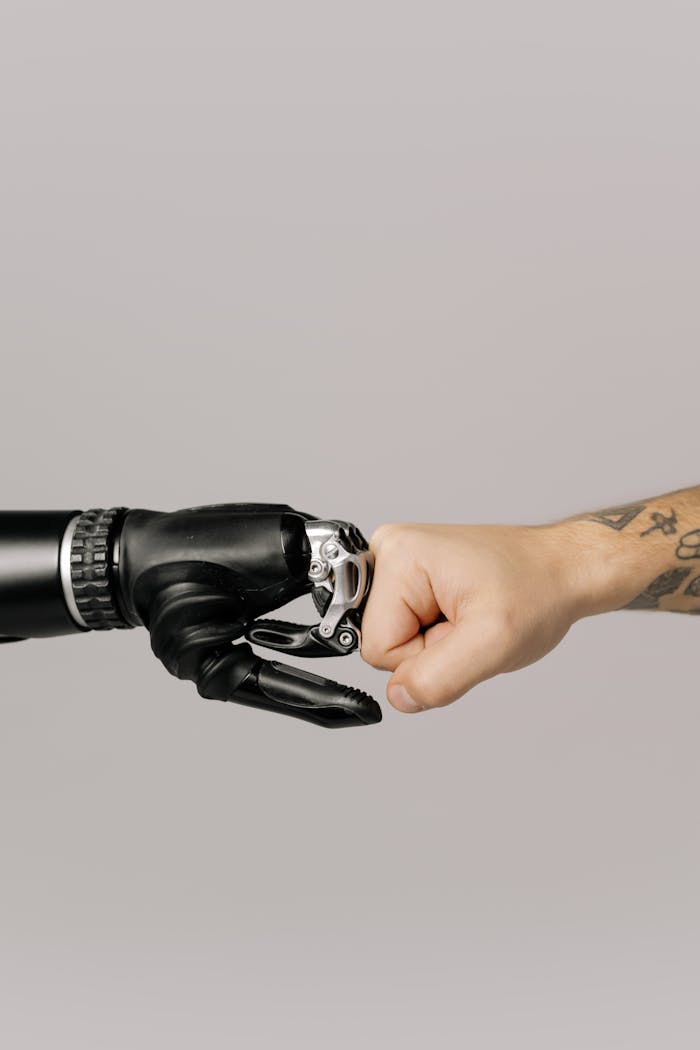 who-we-are Close-up of a human fist bumping a prosthetic hand, symbolizing technology and human connection.